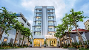 Un hôtel à plusieurs étages, doté d’une entrée principale et entouré d’arbres et d’un jardin bien entretenu.