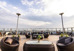 A rooftop terrace with wicker furniture, potted plants, and a view of the city skyline. - THE SQUARE KAMPOT HOTEL (Kampot)