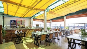 Un espace extérieur aménagé pour les repas, avec des tables et des chaises, un bar doté d’un réfrigérateur et une vue sur la ville.