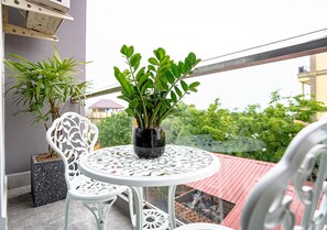 A balcony with a round table and two chairs, a potted plant, and a view of greenery. - THE SQUARE KAMPOT HOTEL (Kampot)
