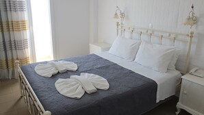 A neatly made bed with white pillows and towels, a white nightstand with a phone, and a wall-mounted light fixture. - Nikolas Hotel (Paros)
