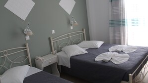 A bedroom with two beds, a nightstand, a lamp, and a window with curtains. - Nikolas Hotel (Paros)