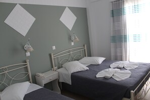 A twin room with two beds, a bedside table with a phone, and a wall-mounted lamp. - Nikolas Hotel (Paros)