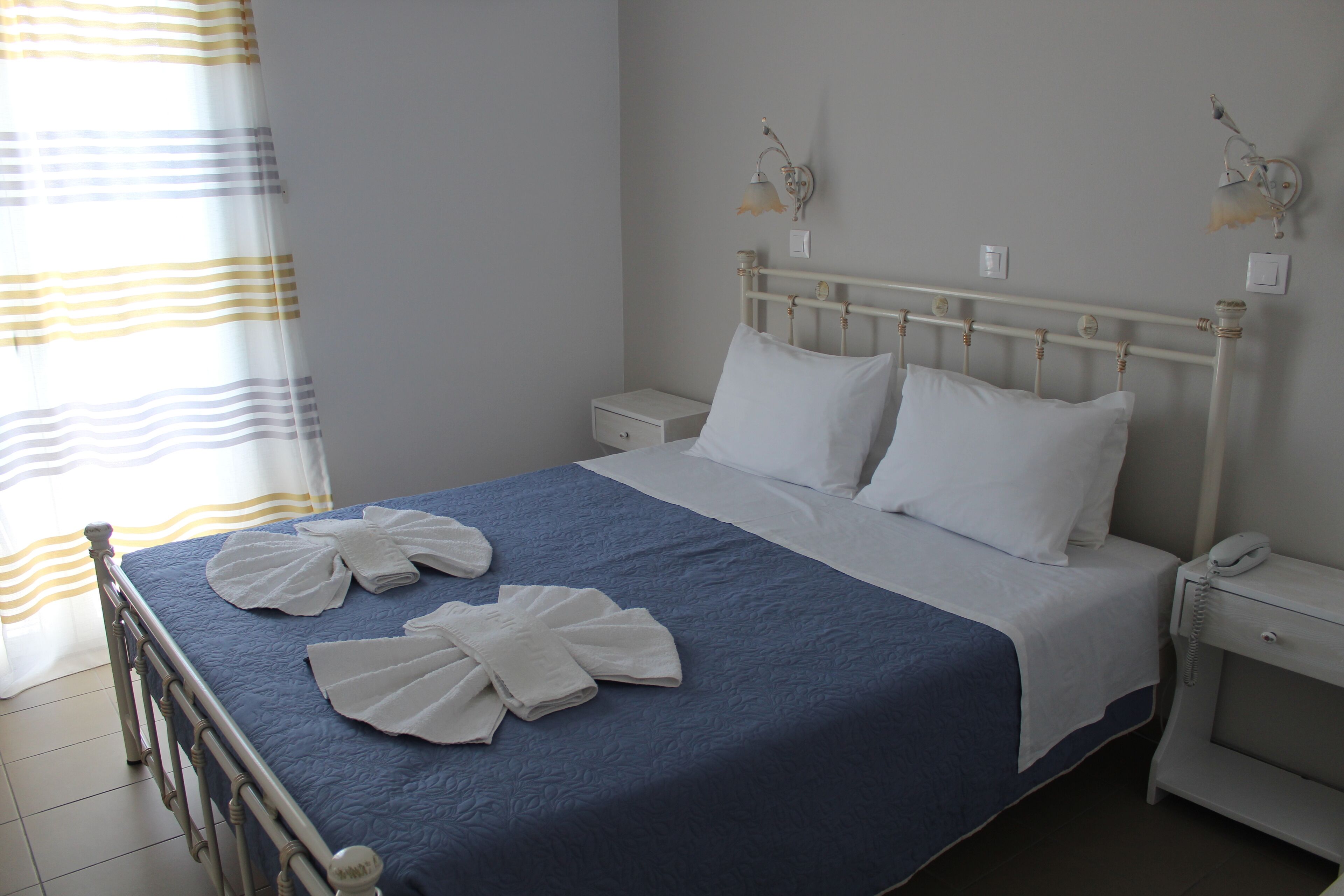 A neatly made bed with white linens, a blue bedspread, and two wall-mounted lamps.