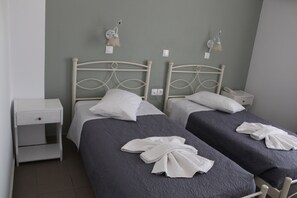 A twin room with two beds, each with a white headboard, a nightstand, and a wall-mounted lamp. - Nikolas Hotel (Paros)
