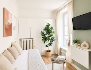 A bedroom with a bed, a potted plant, a radiator, a TV, and a window with curtains. - Cosy studio - Opera Garnier (Paris)
