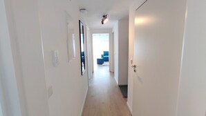 Un pasillo estrecho con paredes blancas, suelo de madera clara y una puerta a la derecha.