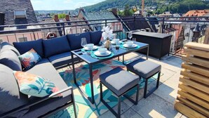 Une terrasse sur le toit avec une table à manger pour quatre personnes, un canapé et un petit coin salon.