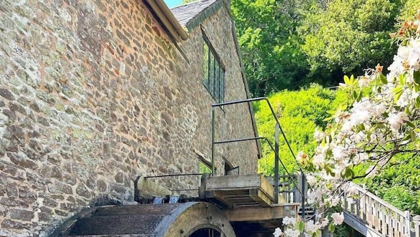 Um edifício de pedra com uma grande roda de água, degraus de madeira e uma cerca de madeira.