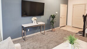 Ein Wohnzimmer mit einem an der Wand befestigten Flachbildfernseher, einem weißen Konsolentisch mit Blumenvase und einer Zimmerpflanze.