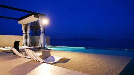 An outdoor swimming pool area with lounge chairs and a covered seating area at night.