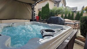 Un bain à remous doté d’un auvent, entouré d’une terrasse en bois et d’une table couverte.