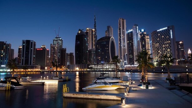 A city skyline at night with illuminated buildings and a marina with boats.