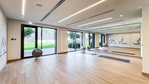 A spacious gym with wooden flooring, exercise mats, and large windows offering a view of greenery.