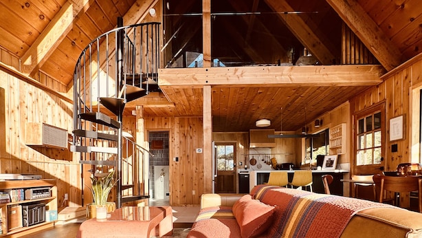 A spacious wooden cabin with a loft bedroom, a dining area, and a kitchen.