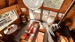 A cozy cabin with a wooden interior, a large window, a sofa, a table, and a fireplace.