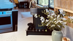 A modern kitchen with a black stove, a white marble countertop, a potted plant, and a glass of milk.
