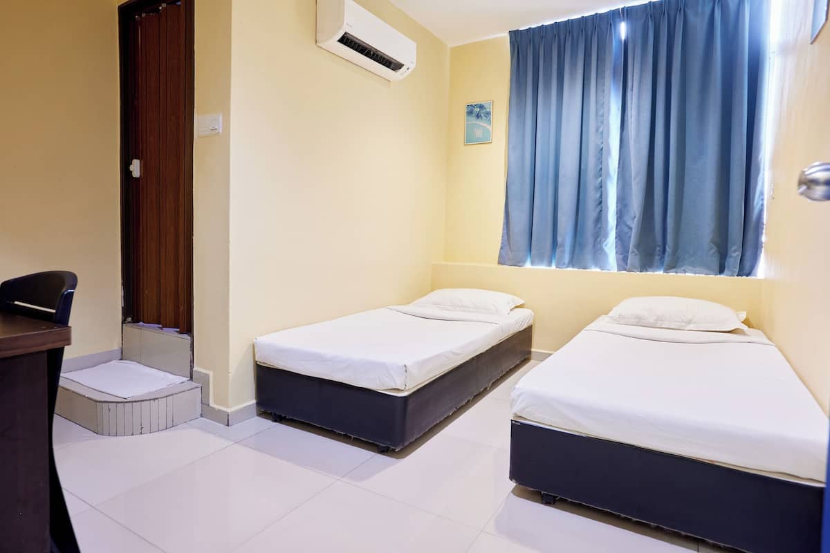 A room with two single beds, a desk, and an air conditioning unit.