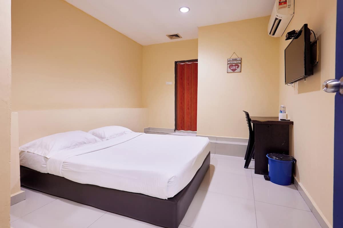 A hotel room with a bed, a desk, a chair, a TV, and a trash bin.