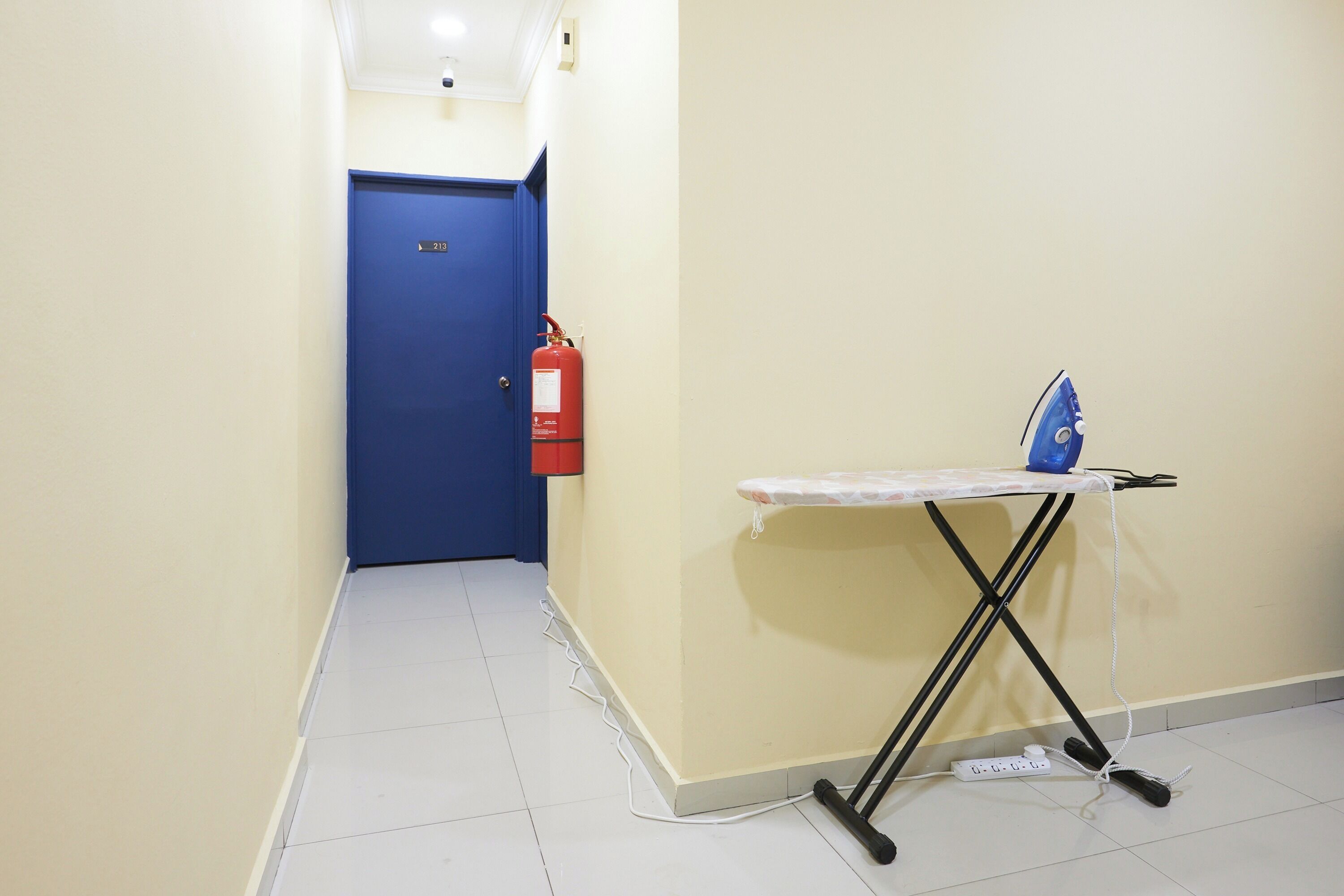 A hallway with a blue door, a fire extinguisher, and an ironing board with an iron.