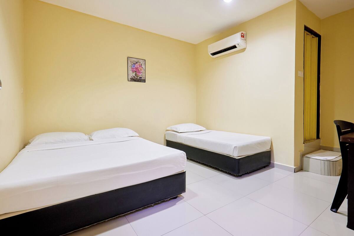 A hotel room with two beds, a small desk, an air conditioning unit, and a mirror.
