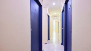 Un couloir d’hôtel avec des portes bleues, des murs blancs et un sol carrelé.