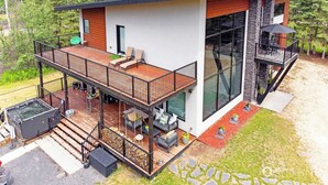 Een modern huis met twee verdiepingen, een houten terras, zitplaatsen buiten en een jacuzzi.