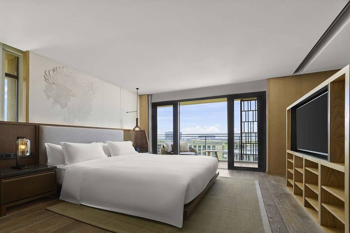 Une chambre d’hôtel moderne avec un grand lit, une table de chevet, un bureau, une carte accrochée au mur, une télévision et un balcon offrant une vue sur la ville.