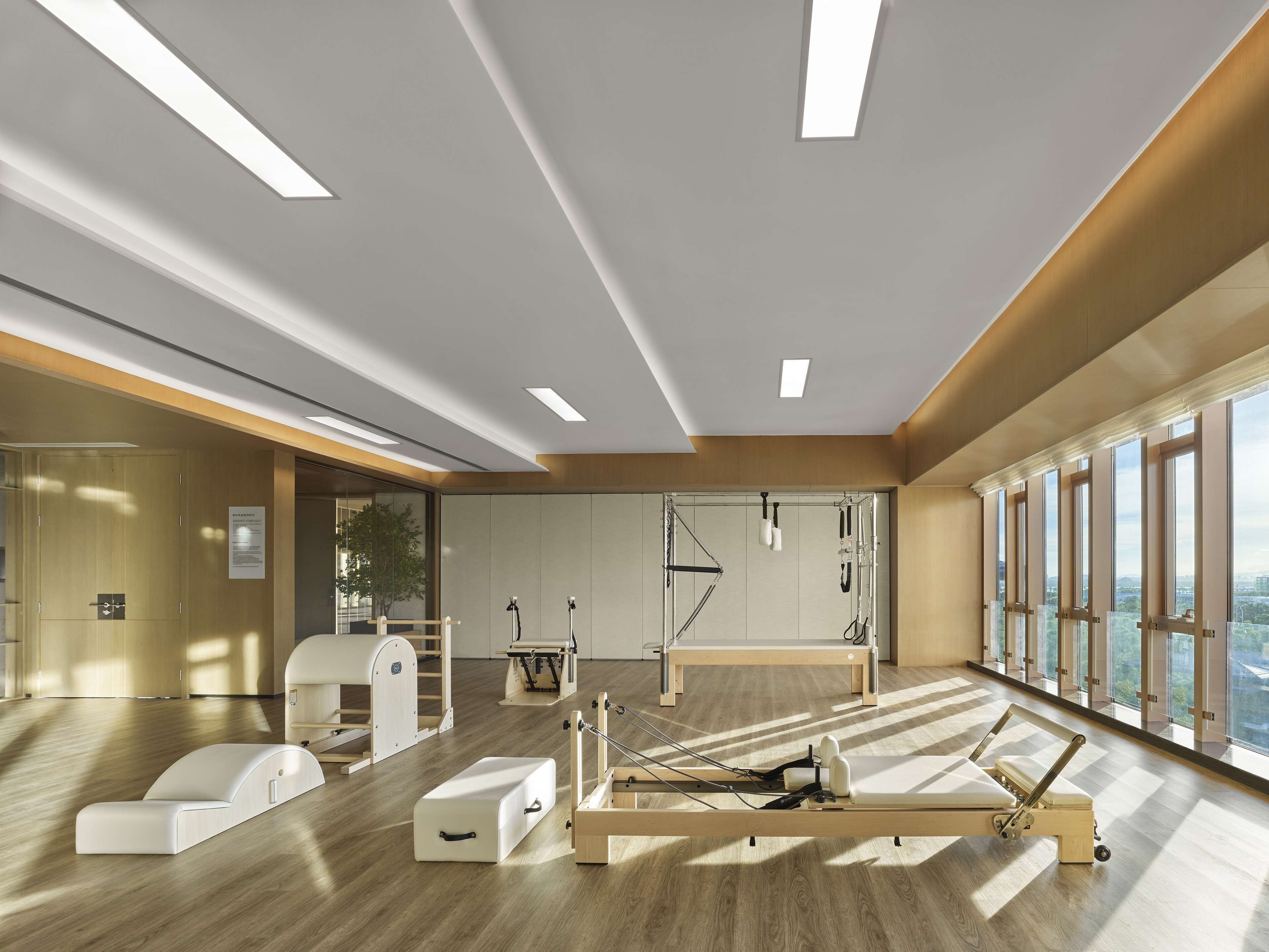 A modern fitness room with exercise equipment, large windows, and a wooden floor.