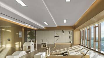 A modern fitness room with exercise equipment, large windows, and a wooden floor.