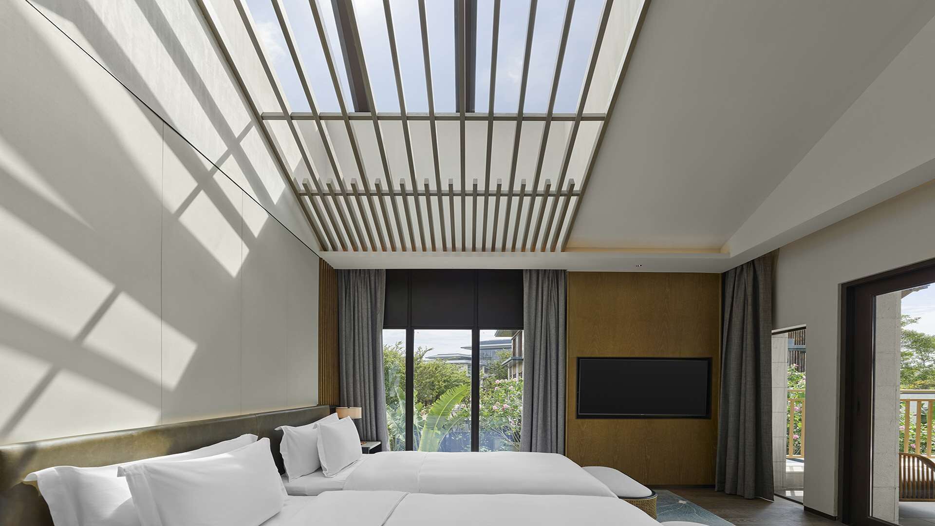 A modern hotel room with a large bed, a flat-screen TV, and a view of greenery outside.