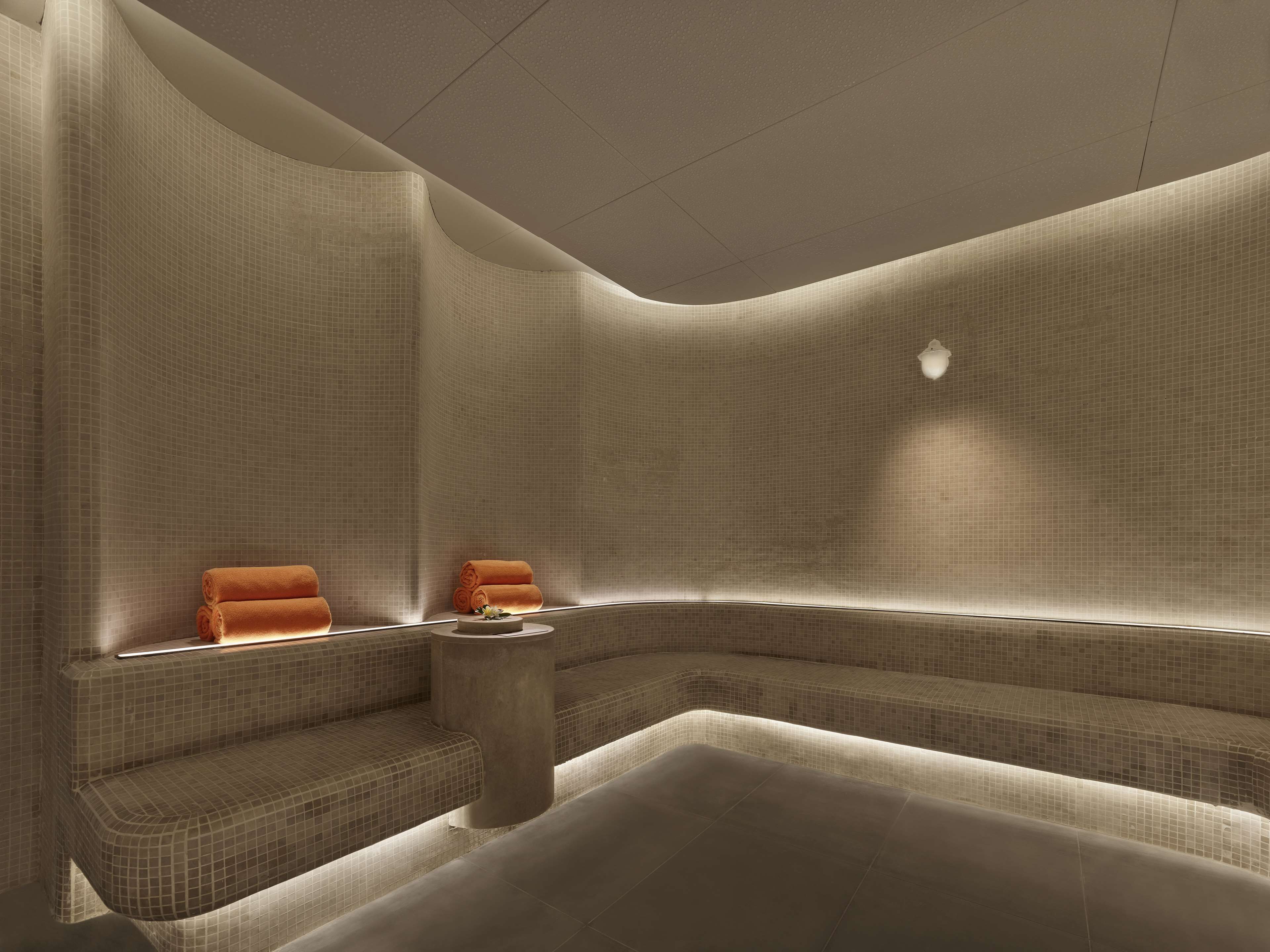 Un moderno spa con un área de asientos curvada, una mesita con un arreglo floral y una lámpara fijada a la pared.