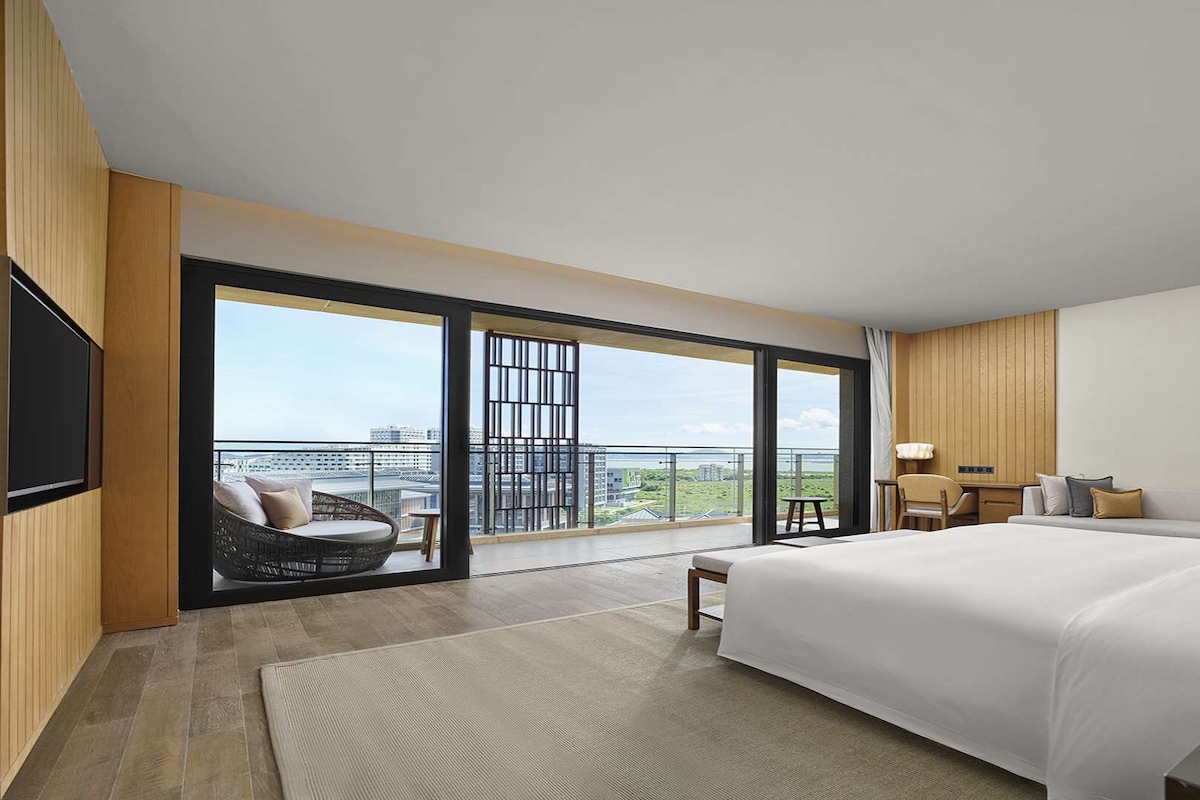 Een moderne hotelkamer met een groot bed, een zithoek met uitzicht en een balkon met stadsgezicht.