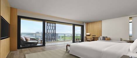 A modern hotel room with a large bed, a seating area with a view, and a balcony with a cityscape view.