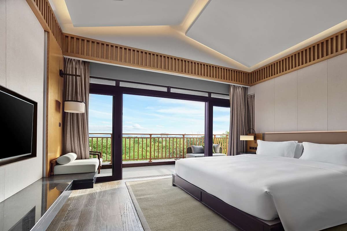 Une chambre d’hôtel moderne dotée d’un grand lit, d’une télévision à écran plat, d’un balcon avec vue et d’une grande fenêtre.