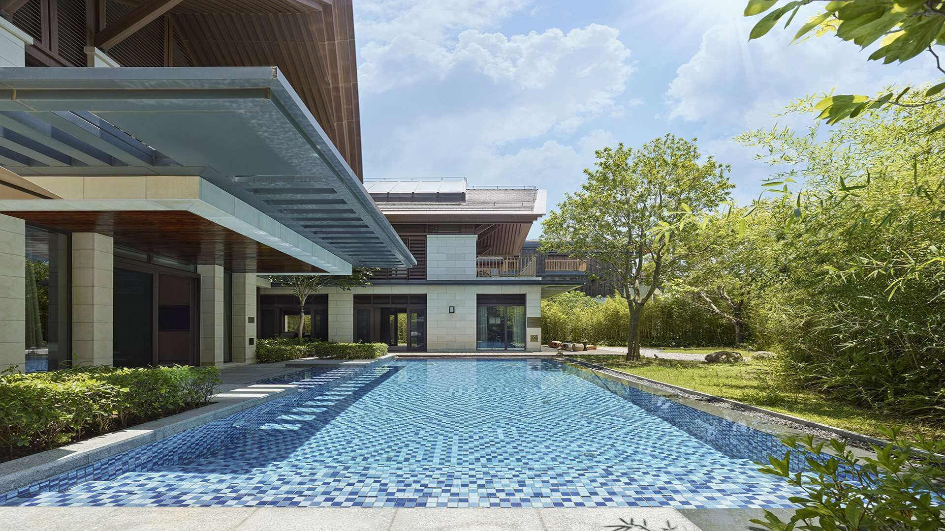 A modern building with a swimming pool, surrounded by greenery and trees.
