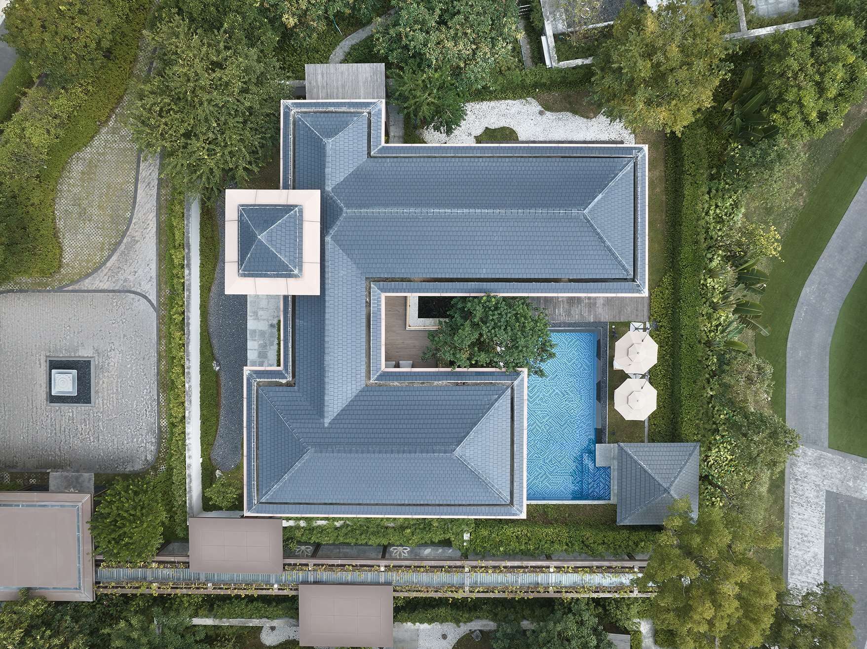 An aerial view of a modern building with a central swimming pool, surrounded by greenery and a covered patio area.