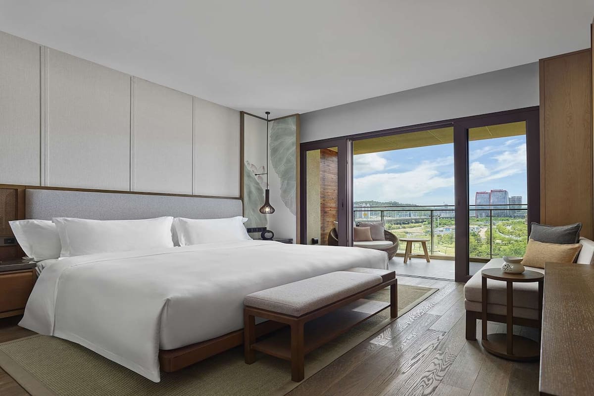 Une chambre d’hôtel moderne dotée d’un grand lit, d’un petit canapé, d’un bureau et d’un balcon offrant une vue sur la ville.
