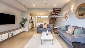 Ein modernes Wohnzimmer mit Flachbildfernseher, grauen Sofas, einem weißen Couchtisch und einer Treppe, die zu einer oberen Ebene führt.