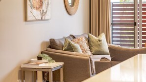Ein Wohnzimmer mit einer Couch, einem kleinen Tisch mit einer Pflanze, einem gerahmten Kunstwerk und einem Spiegel an der Wand.
