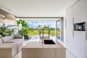 A modern living room with a sofa, a coffee table, and a view of a lush garden.