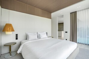 A modern hotel room with a large bed, a bedside lamp, a small round table, and a view of the bathroom.