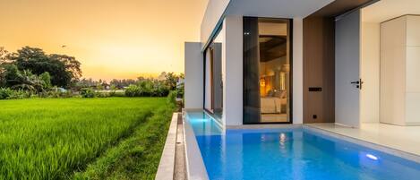 A modern building with a swimming pool, large windows, and a view of a green field.