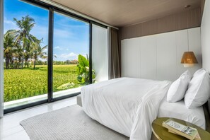 Ein Schlafzimmer mit einem großen Fenster, einem Bett, einem Nachttisch mit einem Buch und einer Lampe.