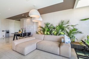 Ein modernes Wohnzimmer mit einer Eckcouch, einem Essbereich mit Tisch und Stühlen sowie verschiedenen Zimmerpflanzen.