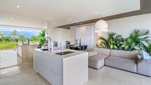 A modern kitchen with a central island, a dining area with a sofa, and a view of the outdoors. - Green Flow Villa 2 with Private Pool in Ubud (Ubud)