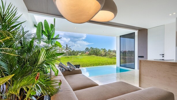 A modern living room with a large sofa, a pool, and a view of a lush garden. - Green Flow Villa 2 with Private Pool in Ubud (Ubud)