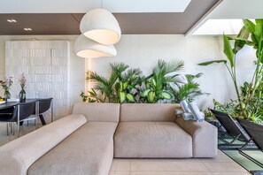 A modern living room with a sectional sofa, a dining area with a table and chairs, and a variety of indoor plants.