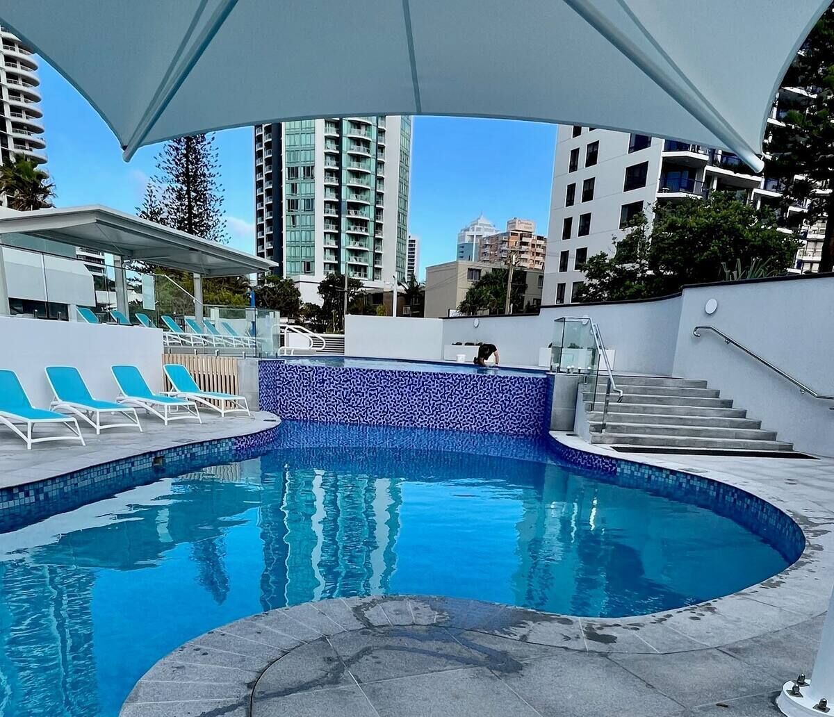 Una piscina con mosaicos azules, sillas de descanso y una escalera que lleva a un nivel superior.