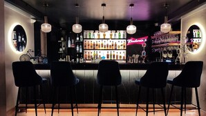 Una zona de bar con un letrero de neón de Budweiser, varias botellas de licor y modernas lámparas colgantes.